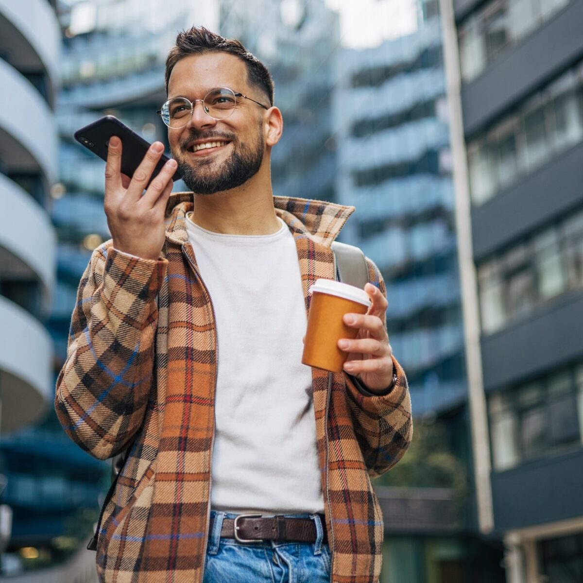Junger Mann mit Brille in der Stadt spricht ins Handy.