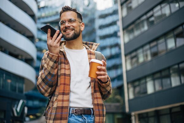 Junger Mann mit Brille spricht am Handy in der Stadt.