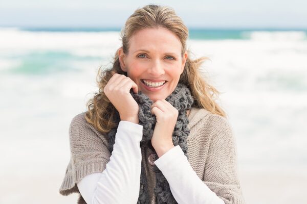 Frau mittleren Alters steht am Meer und blickt in die Kamera.